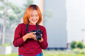 Cheerful young female photographer in casual winter clothes smiling looking at camera screen