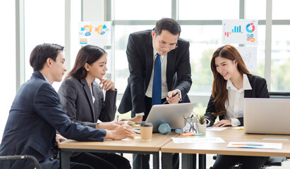 Asian professional successful businessman manager entrepreneur in formal suit standing teaching brainstorming marketing strategy with male female businesswomen employees team in company meeting room