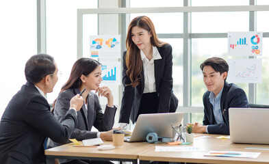 Asian professional successful businesswoman manager entrepreneur in formal suit standing teaching brainstorming marketing strategy with male female businessmen employees team in company meeting room