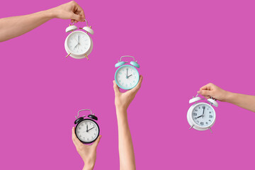Hands holding different alarm clocks on purple background
