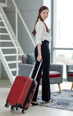Fototapeta na wymiar Portrait shot of Asian professional successful female businesswoman in casual outfit standing smiling looking at camera holding trolley luggage waiting for departure time transportation in airport