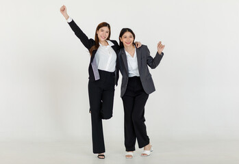 Portrait isolated cutout studio full body shot two Asian professional successful female businesswomen in formal suit standing smiling holding arms smiling together look at camera on white background