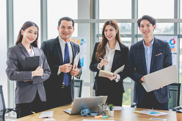 Portrait shot of Asian professional successful group male businessmen and female businesswomen team in formal suit standing together side by side smiling holding laptop textbook clipboard in office