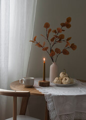 Cozy autumn home interior . Autumn decor, lit candle on a round wooden table in the living room