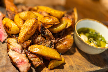 Baked potato wedges with steak and sauce on wooden desk, dish in restaurant