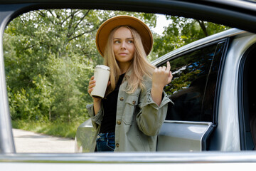 Blonde woman stoped on road next to car and drink coffee or tea from reusable mug. Refuse reuse...