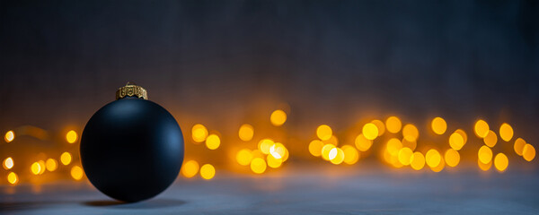 Dark Christmas background with one black bauble and warm cozy bokeh in the background. Christmas and winter holidays background