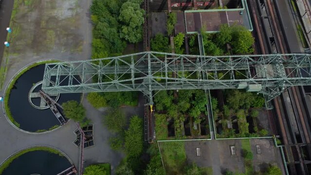 metal bridge construction spanning over grey girders that form an arch shape and are connected by smaller beams circular object which appears to be some kind of wheel or turbine trees plants around