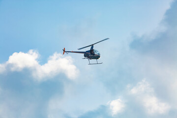 A small helicopter flies through the cloudy sky