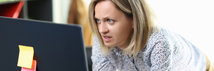 Surprised female manager stands at her working desk and looks at computer screen.