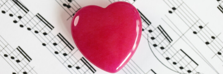 Red heart on paper with musical notes close up.