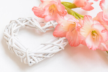 A white weaved heart, pink flowers, blooming pink gladiolus on white background isolated. Love, Valentine ’s Day Concept , copy space