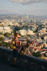 Beautiful view of the capital of Georgia Tbilisi from above from old town. A young man with two dogs admires the sunrise in the city center. Male owner with German and Australian Shepherds.