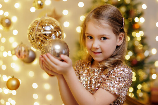 Cute little girl holding golden christmas ball in decorated room