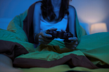 Cropped image of young woman sitting in bed and playing videogame at night - Powered by Adobe