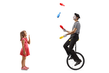 Little girl watching with amusement a mime riding a unicycle and juggling