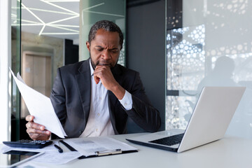 Serious thinking businessman behind paper work inside office, senior mature boss reviewing accounts...