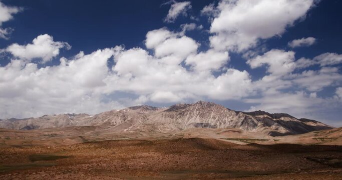 Timelapse mountains. Desert plain with scorched vegetation under blue sky with white fluffy clouds. Arashan. Mountain range in background. Amazing cinematic video for background, ecological agenda