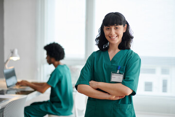 Portrait of smiling medical nurse in green scrubs crossing arms and looking at camera - obrazy, fototapety, plakaty