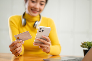 A happy Asian woman holding a credit card and her smartphone, using a mobile banking application.