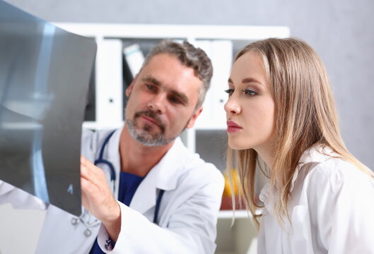 Mature male doctor hold in arm and look at xray photography discussing it with female patient portrait. Bone disease exam medic assistance cancer test healthy lifestyle hospital practice concept