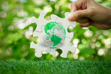 Women's hands holding green earth globe icons on white jigsaw puzzles with nature environment...