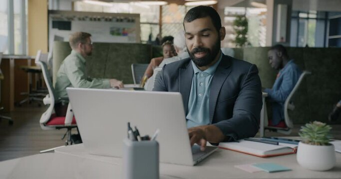 Ambitious Arab man working with laptop typing sitting at desk in modern coworking center. Successful businessman concentrated on corporate activity.