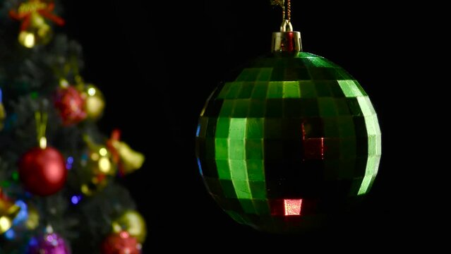 On a black background, a green glossy New Year's ball rotates near a decorated Christmas tree