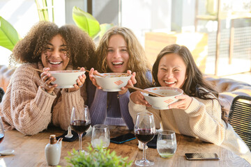 Cheerful diverse female friends eating soup together in cafe