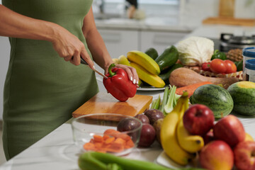 Cropped image of young woman cutting red bell pepper when cooking dinner in kitchen