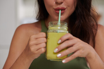 Cropped image of young woman sipping green smoothie