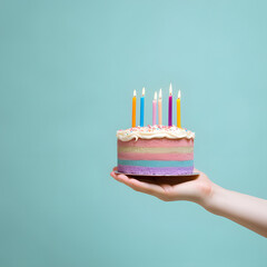 Hand holds a birthday cake with candles on the pastel blue background. Holiday concept art