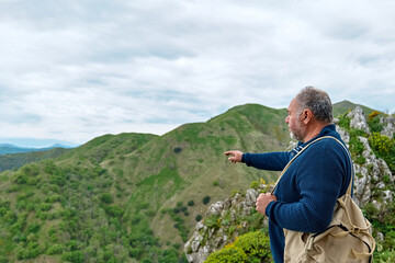 Naklejka na ściany i meble Mature traveler man enjoying freedom on the pick of mountain in front of panoramic view of serene fall nature. Mental health, wellbeing, trip adventure and healthy lifestyle.