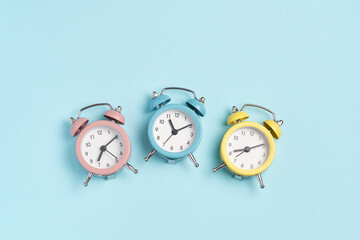 Three alarm clocks of different colors show different times. Start of the day, waking up, morning,...