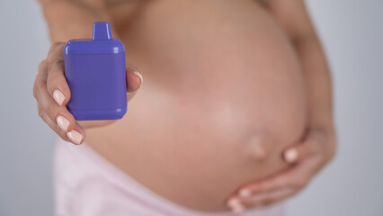 A pregnant woman smokes a vape. A girl holds an electronic cigarette against the background of her...