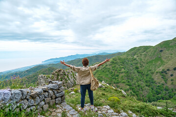 Female traveler spreading arms up to sky enjoying freedom on the pick of mountain with serene fall nature. Mental health, wellbeing, trip adventure and healthy lifestyle.