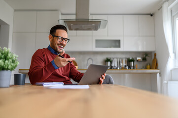 Happy male freelancer discussing over video call on laptop while sitting at desk in home office