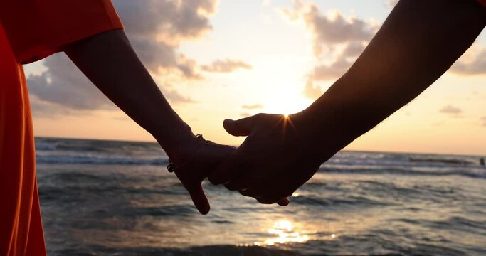 Couple in love holding hands at sunset on beach. Romantic young couple enjoying sun, sun romance and love by sea