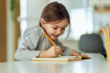 Naklejka na ściany i meble Smiling cute girl using a pen, writing something in her notebook.
