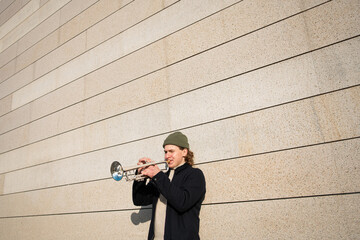 Jazz artist outdoors concert. A man with a hat playing a trumpet next to a brown wall. Male Jazz...