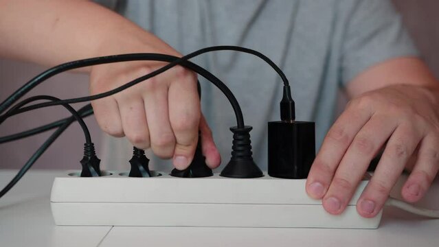 A man plugs a black electrical plug into a surge protector. The concept of electricity consumption, tariffs and cost of electricity. Current consumption by electrical appliances. Close-up