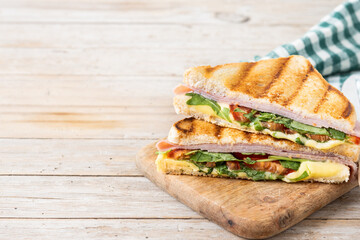 Panini sandwich with ham, cheese, tomato and arugula on wooden table. Copy space