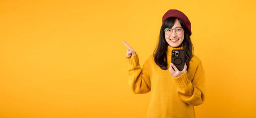 Portrait young beautiful 30s asian woman happy smile wearing yellow shirt and red hat pointing...