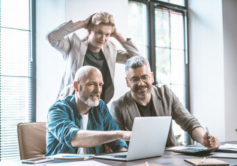 Business team of dedicated men collaborates in modern office, engaged in animated discussion while collectively examining laptop. Teamwork, problem-solving and effective collaboration within corporate