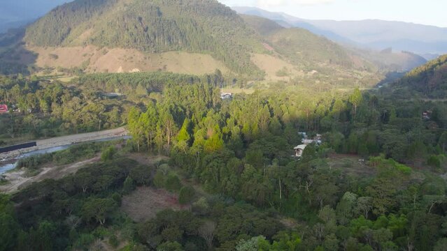 Cinematic daytime drone footage in Oxapampa, Peru. The camera tilts from a downward view towards the horizon, showcasing forested lands and rolling hills.