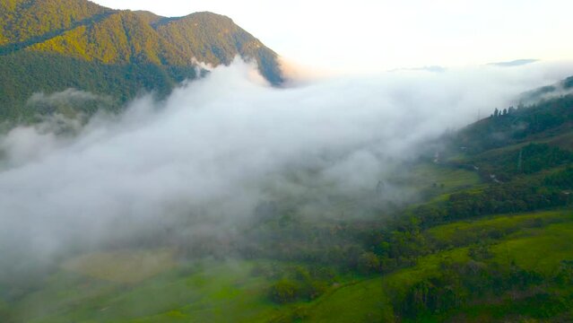 Morning in Oxapampa, Peru, captured from a high-angle drone perspective. A slow, cinematic rotation around the clouds reveals the cloud-covered village, with houses, forested lands, and hills in view.