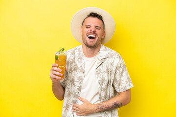 Young caucasian man holding a cocktail isolated on yellow background smiling a lot