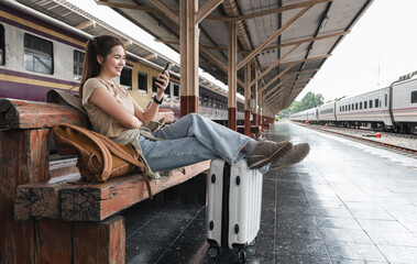 Asian teenage female traveler using her smart phone mobile while waiting for a train at a station