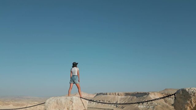 European woman stands against the background of the Negev Desert in Israel is visible in the background over mountains, sandy hills and rock formations. 