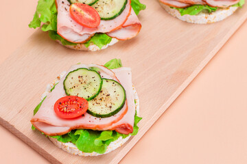 Light Breakfast. Quick and Healthy Sandwiches. Rice Cakes with Ham, Tomato, Fresh Cucumber and Green Salad on Wooden Cutting Board. Beige Background